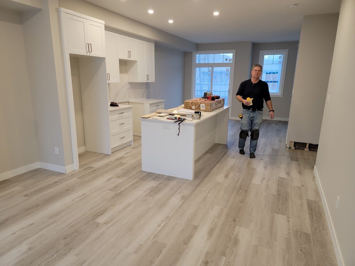 Warwick Interiors installing light grey luxury vinyl plank flooring in a bright, open-concept kitchen with white cabinetry and center island.